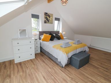 A bedroom with a double bed, bedside tables with lamps, a chest of drawers, and wooden floor at Llwyd Coed Canol in Llanllyfni near Penygroes