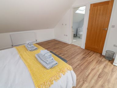 A bedroom with a bed folded towels on a yellow blanket on the bed a wooden floor and an open door leading to a bathroom at Llwyd Coed Canol in Llanllyfni near Penygroes