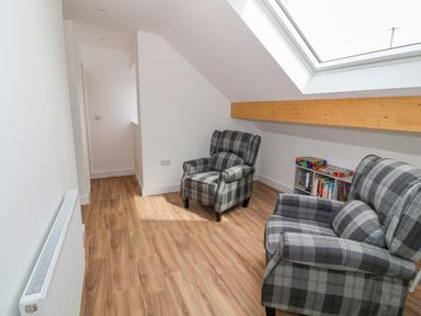 A room with two plaid armchairs a bookshelf with books and games a skylight window and wooden floor at Llwyd Coed Canol Llanllyfni near Penygroes