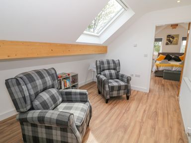 A sitting area with two plaid armchairs a small bookshelf and a skylight window at Llwyd Coed Canol in Llanllyfni near Penygroes