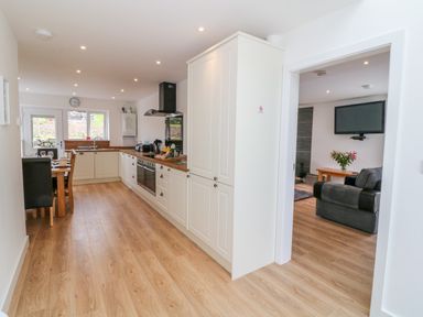 A kitchen with white cabinets and wooden countertops next to a dining table and a living room with a sofa and wall-mounted tv at Llwyd Coed Canol in Llanllyfni near Penygroes
