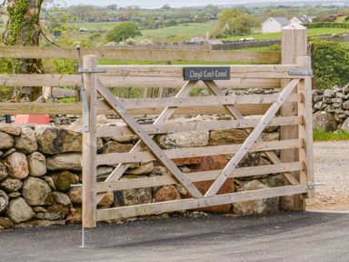 A wooden gate with a sign reading Llwyd Coed Canol in a rural setting with stone walls and green fields at Llwyd Coed Canol in Llanllyfni near Penygroes