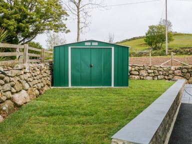 A green metal garden shed on a grassy area surrounded by stone walls at Llwyd Coed Canol in Llanllyfni near Penygroes