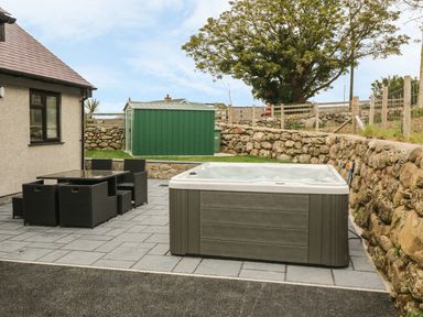 An outdoor patio area with a hot tub black wicker dining table and chairs and a green storage shed at Llwyd Coed Canol in Llanllyfni near Penygroes