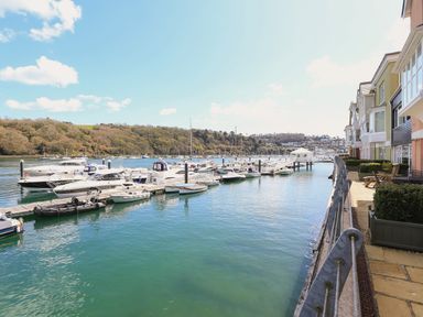 A marina with boats docked along a walkway beside buildings and a hillside in the background at Quayside Dart Marina in Dartmouth