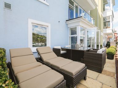 An outdoor patio with two lounge chairs and a dining table set with chairs at Quayside Dart Marina in Dartmouth