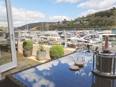 A glass table with champagne bottle and glasses on a balcony overlooking boats at Quayside Dart Marina in Dartmouth