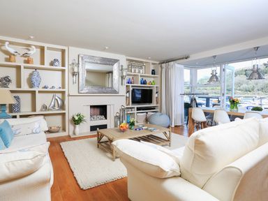 A living room with cream sofas a wooden coffee table a fireplace built in shelves and dining area with large windows at Quayside Dart Marina in Dartmouth