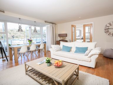 A living room with a white sofa blue cushions a wooden coffee table and a dining table with white chairs and pendant lights at Quayside Dart Marina in Dartmouth