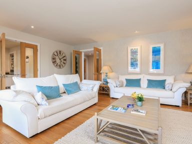 A living room with two white sofas with blue cushions a light wooden coffee table with magazines and a plant a wooden floor and wall art at Quayside Dart Marina in Dartmouth