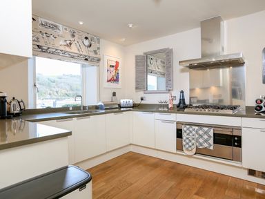 A kitchen with white cabinets wooden floor a window with patterned blind stove oven and kitchen sink at Quayside Dart Marina in Dartmouth