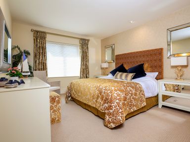 A bedroom with a large bed with patterned bedding two mirrors and a dresser at Quayside Dart Marina in Dartmouth