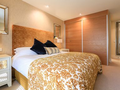 A bedroom with a bed covered in a patterned bedspread two black pillows wooden sliding closet doors and two bedside tables with lamps at Quayside Dart Marina in Dartmouth