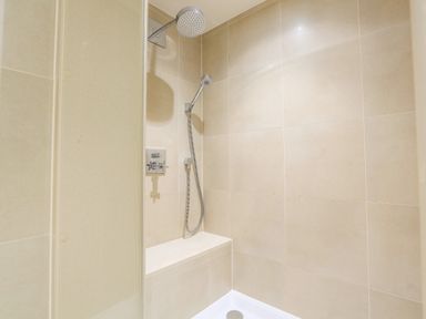 A shower area with a wall-mounted rain shower head handheld shower and a built-in tiled bench at Quayside Dart Marina in Dartmouth