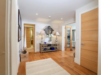 A hallway with wooden floor a console table with two lamps a round mirror flowers and decorative items at Quayside Dart Marina Dartmouth