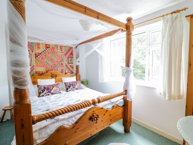 A bedroom with a wooden four poster bed and a window with white curtains at Dyfi Cottage in Dolgellau