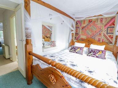 A bedroom with a wooden four poster bed and patterned wall hanging at Dyfi Cottage in Dolgellau