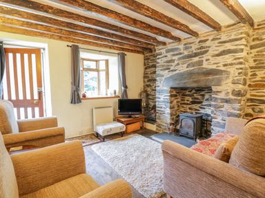 A living room with two armchairs a sofa a small television on a table a stone fireplace and wooden ceiling beams at Dyfi Cottage in Dolgellau