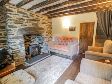 A living room with a stone fireplace wooden beams on the ceiling a sofa armchairs a rug and a wooden door at Dyfi Cottage in Dolgellau