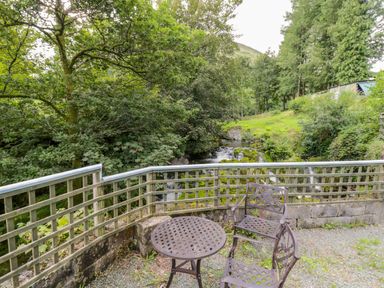 A patio with metal table and chairs overlooking a stream and trees at Dyfi Cottage in Dolgellau