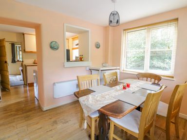 A dining room with a wooden table and six chairs near a window with blinds at Dyfi Cottage in Dolgellau