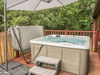 A hot tub with steps and a patio umbrella on a wooden deck surrounded by trees at 40 Skiptory Howe in Troutbeck Bridge