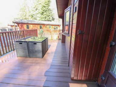 An outdoor wooden deck with a rattan table and chairs near a wooden cabin at 40 Skiptory Howe in Troutbeck Bridge