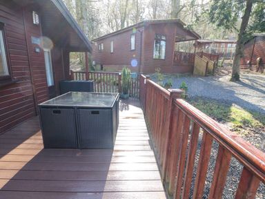 A wooden deck with a glass top table and two black chairs outside a wooden cabin at 40 Skiptory Howe in Troutbeck Bridge
