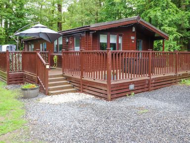 A wooden cabin with a wraparound deck and steps in a wooded area at 40 Skiptory Howe in Troutbeck Bridge