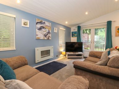 A living room with two sofas a wall-mounted fireplace a television on a stand and windows at 40 Skiptory Howe in Troutbeck Bridge