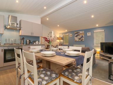 An open plan kitchen and dining area with a wooden table set for six and a living room with a TV at 40 Skiptory Howe in Troutbeck Bridge