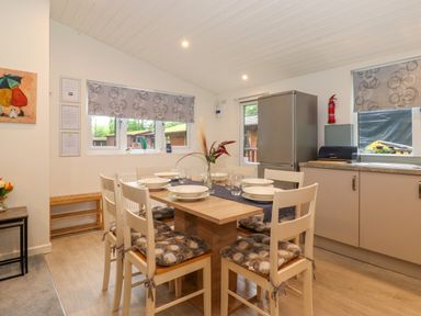 A dining area with a wooden table and six chairs set with plates and glasses beside a kitchen with cabinets and a refrigerator at 40 Skiptory Howe in Troutbeck Bridge