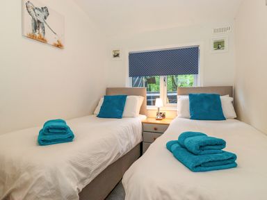 A bedroom with two single beds blue towels and pillows a window with blue blinds and a bedside table lamp at 40 Skiptory Howe in Troutbeck Bridge