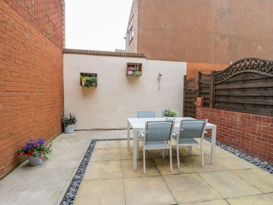 A small paved patio with a white table and four chairs surrounded by brick walls and small potted plants at Valiant House Scarborough
