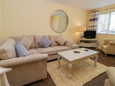 A living room with a beige sofa, coffee table, armchair, television on a stand and window at Valiant House in Scarborough