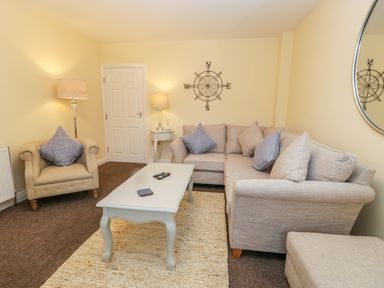 A living room with a beige armchair and a corner sofa with cushions a white coffee table and two lamps at Valiant House in Scarborough