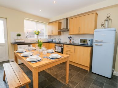A kitchen with wooden cabinets a light blue fridge a wooden dining table set with plates bowls glasses and cutlery at Valiant House in Scarborough