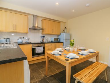 A kitchen with wooden cabinets black countertop dining table set for six with dishes and glasses at Valiant House in Scarborough