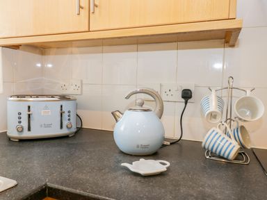 A kitchen counter with a light blue toaster a matching kettle a set of four hanging striped mugs and wooden cabinets above at Valiant House Scarborough