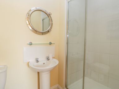 A bathroom with a round mirror above a pedestal sink and a glass shower enclosure at Valiant House in Scarborough
