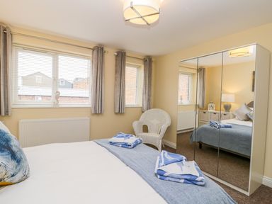 A bedroom with a bed a wicker chair mirrored wardrobe and two windows at Valiant House in Scarborough