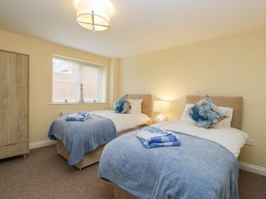 A bedroom with two single beds with blue blankets and pillows a wooden wardrobe and a window at Valiant House Scarborough