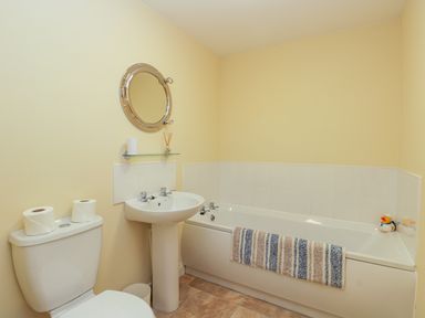 A bathroom with a toilet, pedestal sink, bathtub with a striped towel hanging and a round mirror on the wall at Valiant House in Scarborough