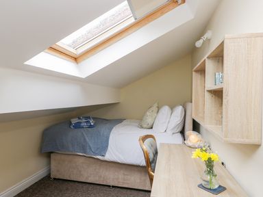 A small bedroom with a single bed under a skylight and a desk with a chair and flowers at Valiant House in Scarborough