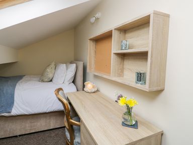 A bedroom with a bed desk chair wall shelves and flowers on the desk at Valiant House in Scarborough