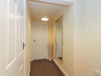 A hallway with closed white doors a hanging light a tall mirror on the wall and a vase with dried decorative grass at Valiant House in Scarborough