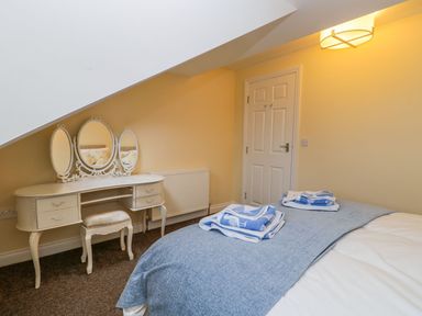 A bedroom with a bed with folded towels a dressing table with three mirrors and a stool at Valiant House Scarborough