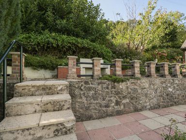 An outdoor stone stairway leading to a patio with a low stone and brick wall surrounded by greenery at Tudor House in Symonds Yat