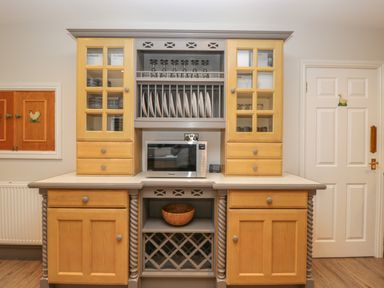 A kitchen cabinet with glass doors plates glasses microwave and wooden bowl at Tudor House in Symonds Yat