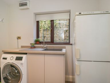 A utility room with a washing machine, sink, countertop, window, and refrigerator at Tudor House in Symonds Yat